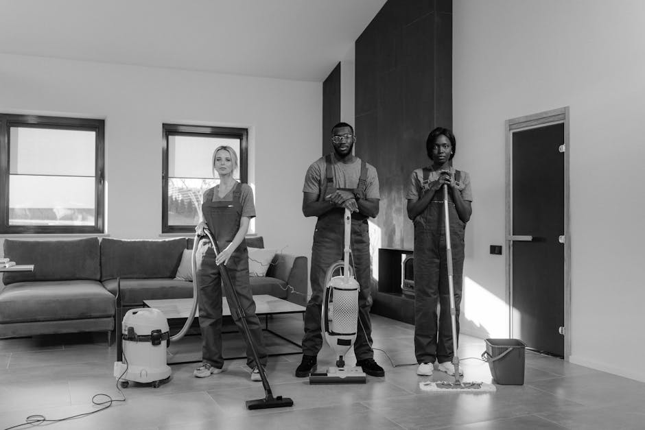 Three professional cleaners from Richmond upon Thames Carpet Cleaners stand in a modern living room, equipped with various cleaning tools including a vacuum cleaner, a mop, and a spray bottle. The roo